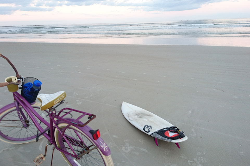 Purple bike and surfboard on beach
